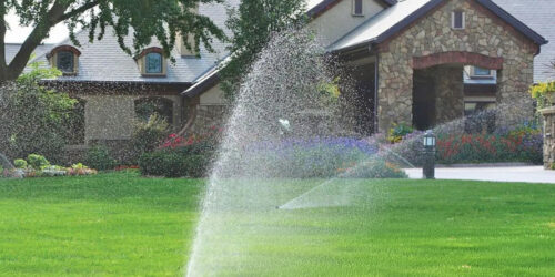 Sprinklers spraying water on yard getting overspray on a house